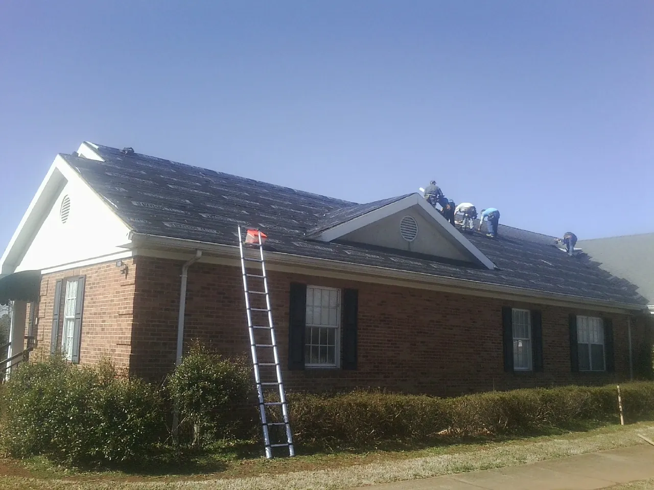 Crew tearing shingles off a brick ranch roof with a ladder set — Emergency Roof Repair work by our crew in Sadieville
