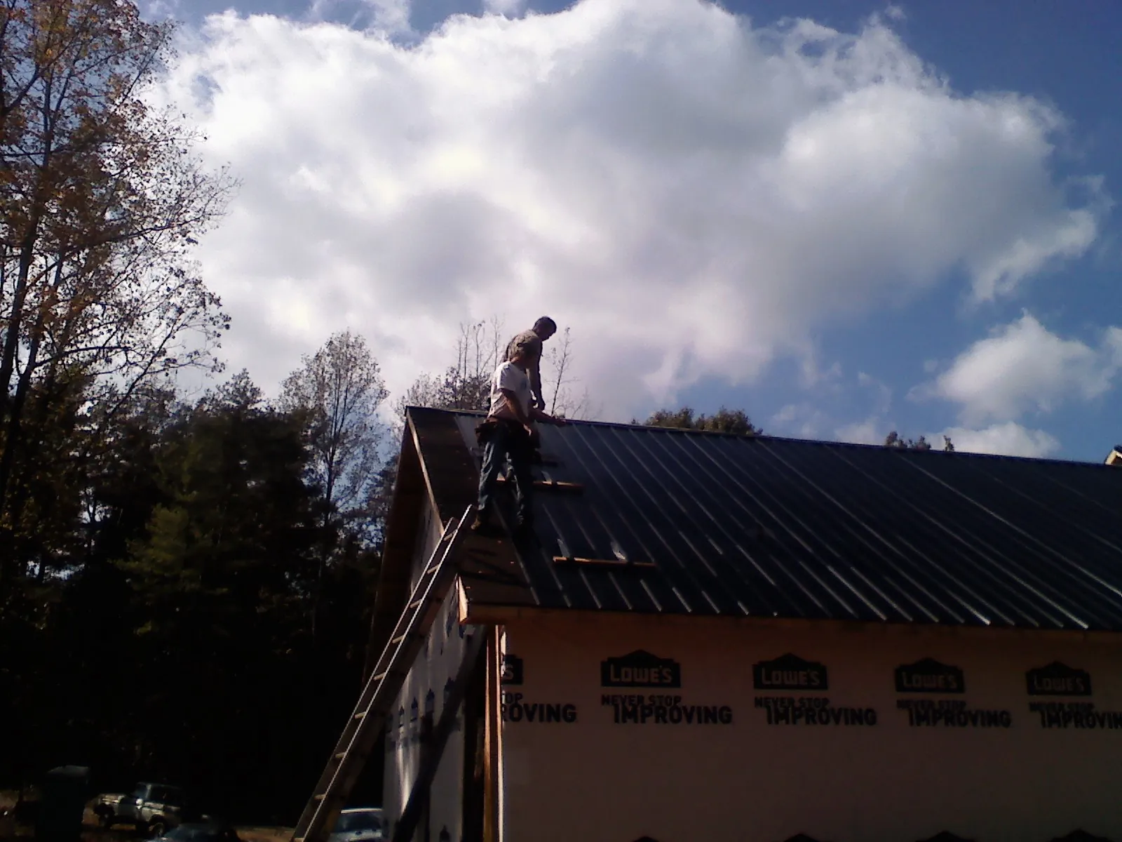 Roofer fastening dark metal panels high against a cloudy sky, from a Roof Inspection job in Sadieville