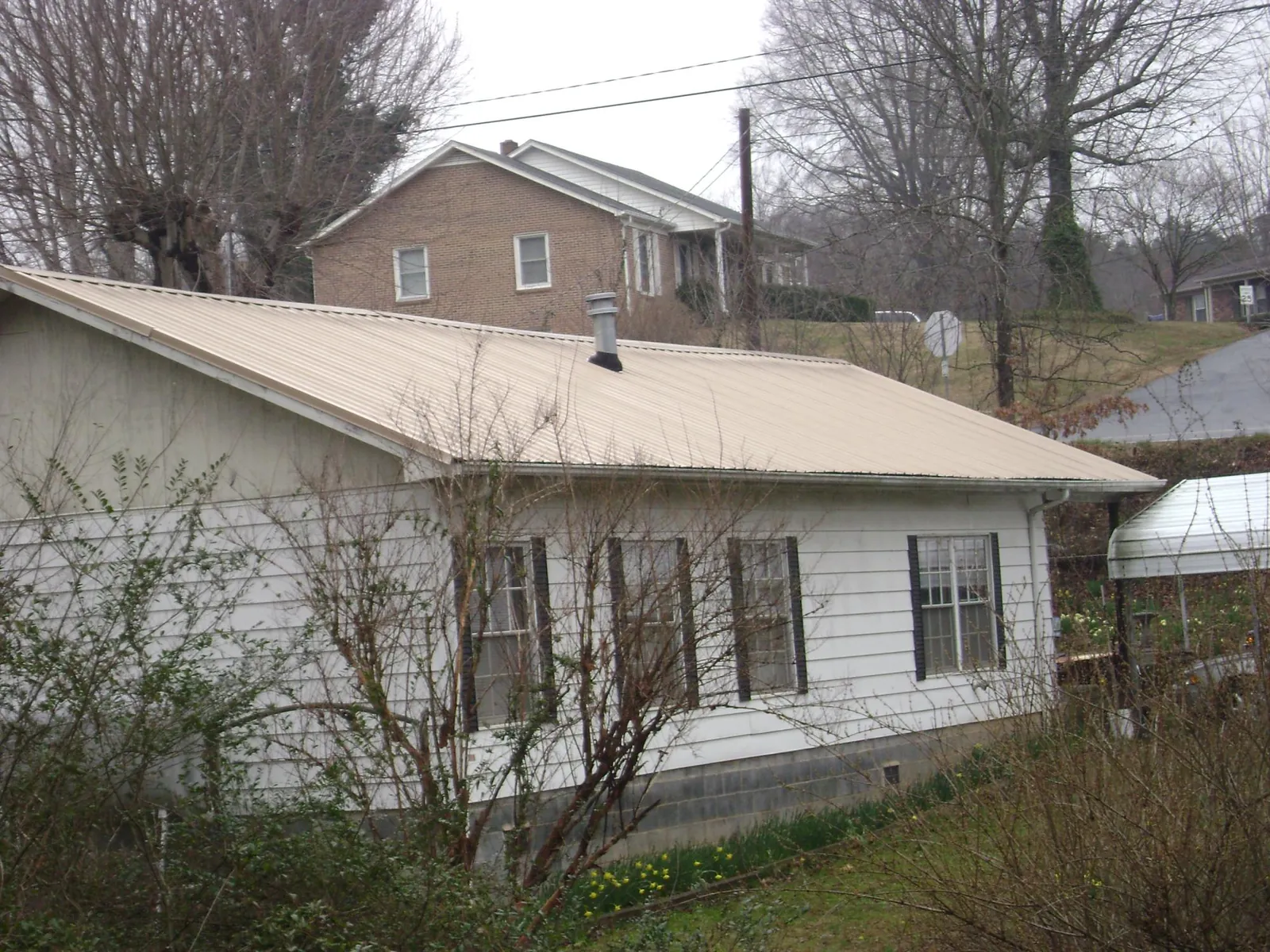 Tan metal roof on a white sided house set into a hillside — Commercial Roofing by Roofing Brothers in Sadieville